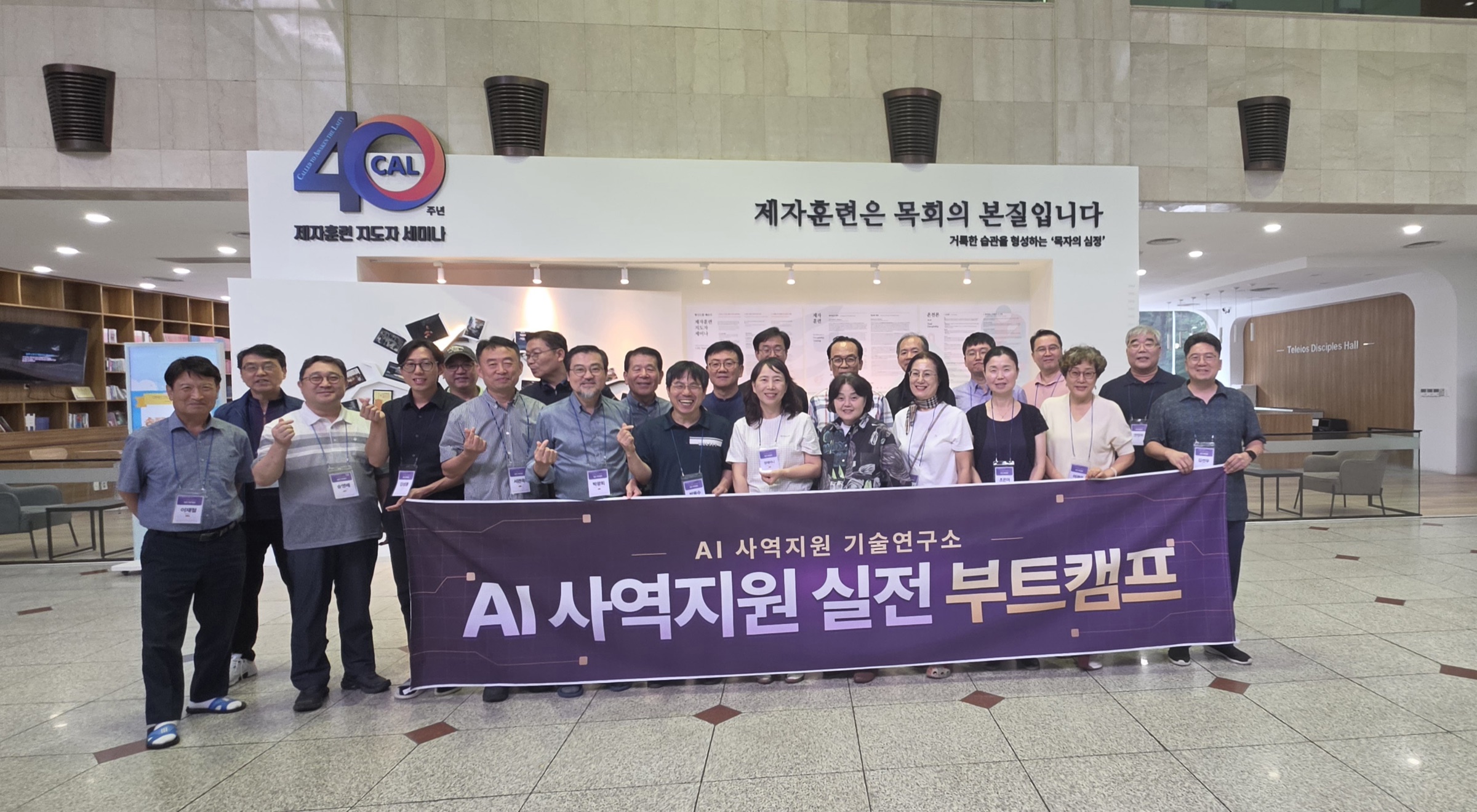 세미나 건물 로비에서 서른 명 남짓한 참여자들이 'AI 사역지원 기술연구소 · AI 사역지원 실전 부트캠프'라고 쓰인 자보라색 현수막을 함께 들고 나란히 서 있다.