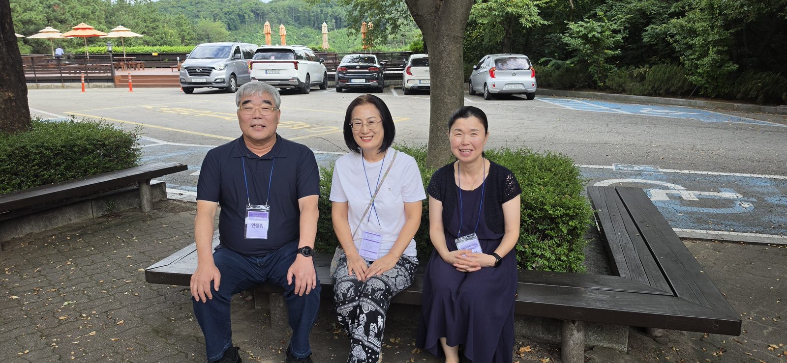 건물 밖 낮은 담에 세 사람이 나란히 앉아 웃고 있다.