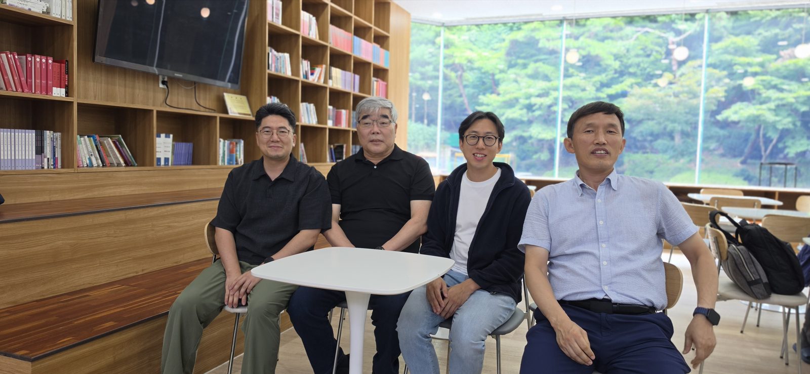 도서관 책장 앞 둥근 탁자에 네 사람이 둘러앉아 사진을 찍었다.